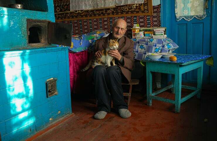 uomo anziano seduto in cucina coccola gatto